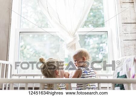 Two sisters, a baby and a toddler, play together in a crib by a window; Sorrento, British Columbia, Canada View Large Photo Image Stock Photograph - Two sisters, a baby and a toddler, play together in a crib by a window; Sorrento, British Columbia, Canada. Fotosearch