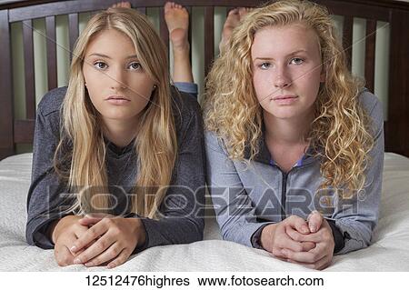 Stock Photograph - Two teenage girls with blond hair laying on a bed and posing for the camera; Connecticut, United States of America. Fotosearch