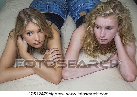 Stock Photograph - Two teenage girls with blond hair laying on a bed; Connecticut, United States of America. Fotosearch