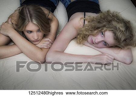 Stock Photograph - Two teenage girls with blond hair laying on a bed looking bored; Connecticut, United States of America. Fotosearch