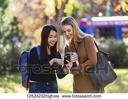 Two university student friends stand together on a university campus looking at a smart phone; Edmonton, Alberta, Canada View Large Photo Image Stock Photograph - Two university student friends stand together on a university campus looking at a smart phone; Edmonton, Alberta, Canada. Fotosearch
