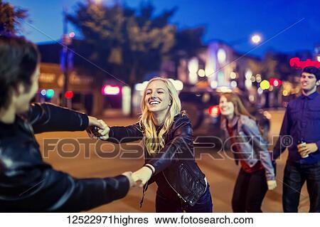 Stock Photograph - Two young couples being playful on the sidewalk beside a city street at dusk; Edmonton, Alberta, Canada. Fotosearch