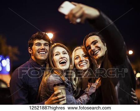 Two young couples stand closely together on the street at nighttime to pose for a self-portrait with a smart phone; Edmonton, Alberta, Canada View Large Photo Image Stock Photograph - Two young couples stand closely together on the street at nighttime to pose for a self-portrait with a smart phone; Edmonton, Alberta, Canada. Fotosearch