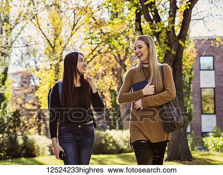 Stock Photograph - Two young female student friends walk and talk together on a university campus; Edmonton, Alberta, Canada. Fotosearch