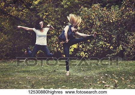 Two young girls kicking up their heels and leaping and dancing in a park in the evening during the fall; Edmonton, Alberta, Canada View Large Photo Image Stock Photograph - Two young girls kicking up their heels and leaping and dancing in a park in the evening during the fall; Edmonton, Alberta, Canada. Fotosearch