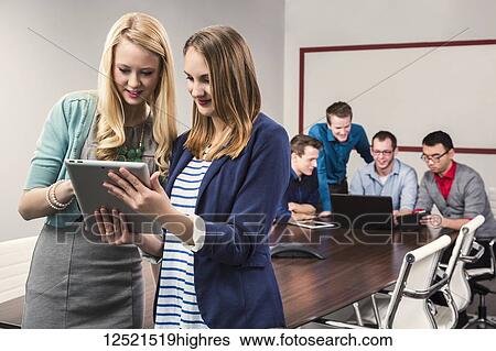 Two young millennial business professionals looking at a tablet while working together in a conference room with their peers; Sherwood Park, Alberta, Canada View Large Photo Image Stock Photograph - Two young millennial business professionals looking at a tablet while working together in a conference room with their peers; Sherwood Park, Alberta, Canada. Fotosearch