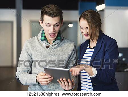 Two young millennial business professionals surpirsed by what they see on the tablet at their place of work; Sherwook Park, Alberta, Canada View Large Photo Image Stock Photograph - Two young millennial business professionals surpirsed by what they see on the tablet at their place of work; Sherwook Park, Alberta, Canada. Fotosearch