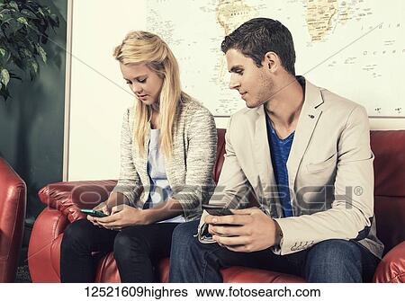 Stock Photograph - Two young millennial business professionals in the lobby of their workplace using their smart phones while taking a break; Sherwood Park, Alberta, Canada. Fotosearch