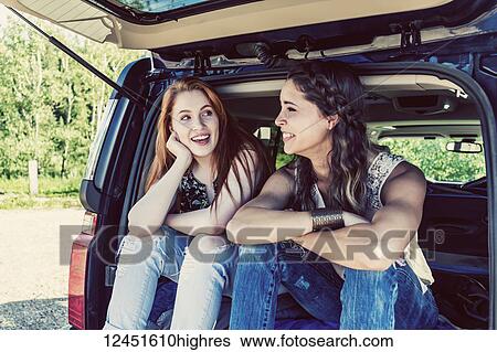 Two young women on a road trip sit in the back of a vehicle talking and laughing together; Edmonton, Alberta, Canada View Large Photo Image Stock Photograph - Two young women on a road trip sit in the back of a vehicle talking and laughing together; Edmonton, Alberta, Canada. Fotosearch