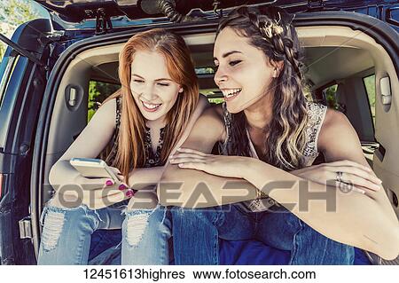 Two young women on a road trip sit in the back of a vehicle using a smart phone; Edmonton, Alberta, Canada View Large Photo Image Stock Photograph - Two young women on a road trip sit in the back of a vehicle using a smart phone; Edmonton, Alberta, Canada. Fotosearch