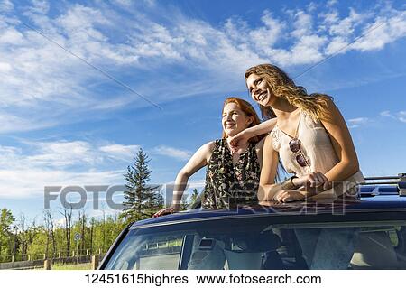 Two young women on a road trip stand up in the sunroof of a vehicle looking out; Edmonton, Alberta, Canada View Large Photo Image Stock Photograph - Two young women on a road trip stand up in the sunroof of a vehicle looking out; Edmonton, Alberta, Canada. Fotosearch