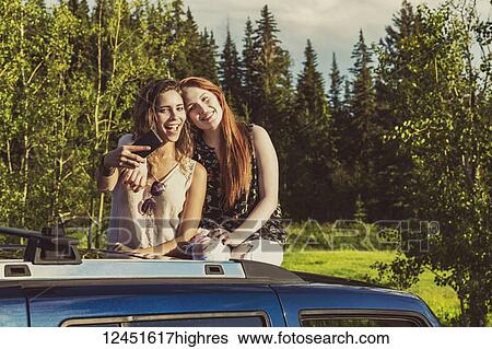 Two young women on a road trip stand up in the sunroof of a vehicle taking a self-portrait with a smart phone; Edmonton, Alberta, Canada View Large Photo Image Stock Photograph - Two young women on a road trip stand up in the sunroof of a vehicle taking a self-portrait with a smart phone; Edmonton, Alberta, Canada. Fotosearch