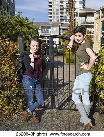 Two young women stand leaning against a metal gate looking confident and cool with housing in the background; New Westminster, British Columbia, Canada View Large Photo Image Stock Photograph - Two young women stand leaning against a metal gate looking confident and cool with housing in the background; New Westminster, British Columbia, Canada. Fotosearch