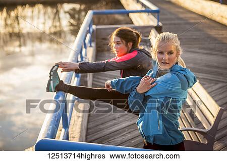 Stock Photograph - Two young women stretching on a trail at the water's edge; Anchorage, Alaska, United States of America. Fotosearch