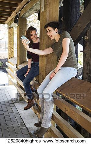 Two young women using a smart phone and being silly taking a self-portrait; New Westminster, British Columbia, Canada View Large Photo Image Stock Photograph - Two young women using a smart phone and being silly taking a self-portrait; New Westminster, British Columbia, Canada. Fotosearch