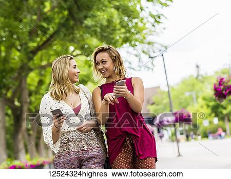 Two young women walk down a path on a university campus laughing and talking together as they look at their smart phones; Edmonton, Alberta, Canada View Large Photo Image Stock Photograph - Two young women walk down a path on a university campus laughing and talking together as they look at their smart phones; Edmonton, Alberta, Canada. Fotosearch