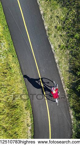 Stock Photograph - View from directly above a cyclist in a red shirt on a paved cycling trail; Calgary, Alberta, Canada. Fotosearch