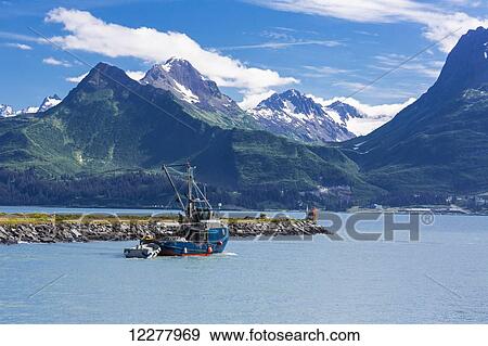 Stock Photo - View of a seine fishing boat leaving the Valdez boat harbor and the Chugach Mountain Range, Southcentral Alaska, Summer.. Fotosearch