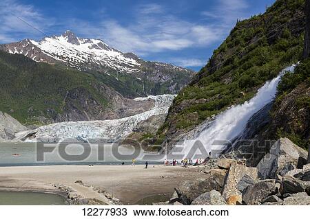 Stock Image - View of tourists standing near Nugget Falls by the Mendenhall Glacier, Juneau, Southeast Alaska, Summer.. Fotosearch