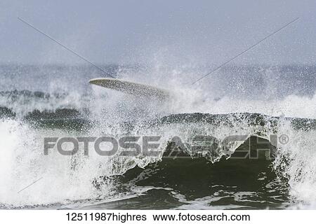 Stock Photograph - Waves breaking and crashing near shore with a surfboard in the splashing water on top of the wave; Tofino, British Columbia, Canada. Fotosearch