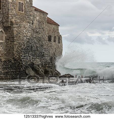 Stock Photograph - Waves crashing and splashing against the old stone walls along the coast of Budva; Budva, Opstina Budva, Monte. Fotosearch