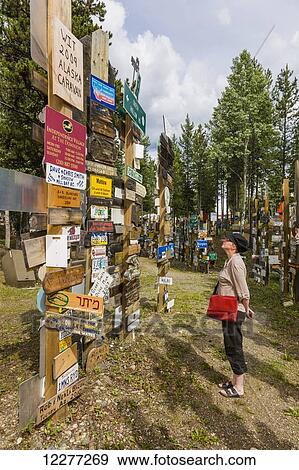 Stock Photo - Woman explores the Signpost Forest, Watson Lake, Yukon Territory, Canada, summer. Fotosearch
