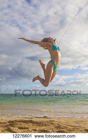 Woman in a bikini leaping in the air on the beach; Kailua, Island of Hawaii, Hawaii, United States of America View Large Photo Image Stock Image - Woman in a bikini leaping in the air on the beach; Kailua, Island of Hawaii, Hawaii, United States of America. Fotosearch