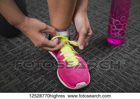 Stock Photograph - Woman tying a green shoelace on a pink running shoe while working out; Spruce Grove, Alberta, Canada. Fotosearch