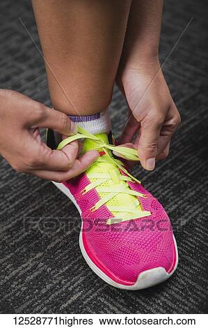 Stock Photograph - Woman tying a green shoelace on a pink running shoe while working out; Spruce Grove, Alberta, Canada. Fotosearch