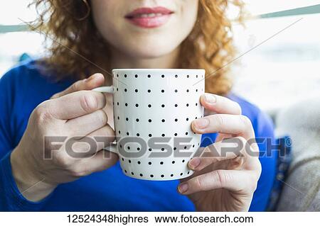 Stock Photograph - Woman with red, curly hair holding a polka dotted mug; Surrey, British Columbia, Canada. Fotosearch