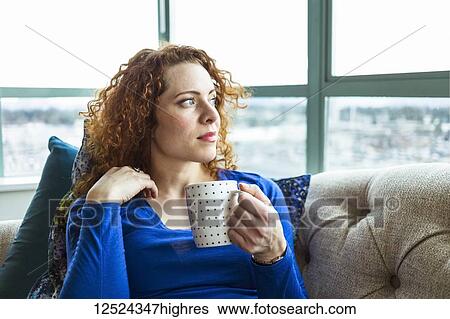 Stock Photograph - Woman with red, curly hair sitting with a mug looking out the window; Surrey, British Columbia, Canada. Fotosearch