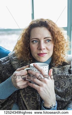 Stock Photograph - Woman with red, curly hair sitting with a mug by a window; Surrey, British Columbia, Canada. Fotosearch