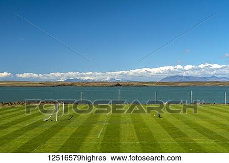Stock Photograph - Young boy playing football on pitch beside the sea; Borganes, Iceland. Fotosearch