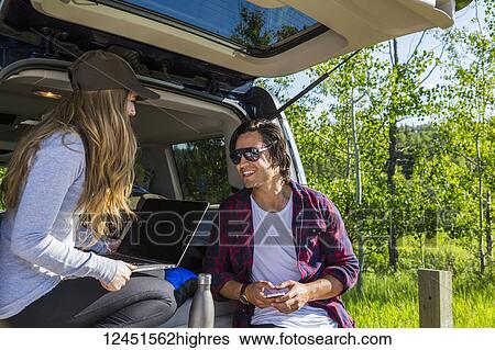 Stock Photograph - Young couple at their vehicle with the back open looking at a laptop computer; Edmonton, Alberta, Canada. Fotosearch