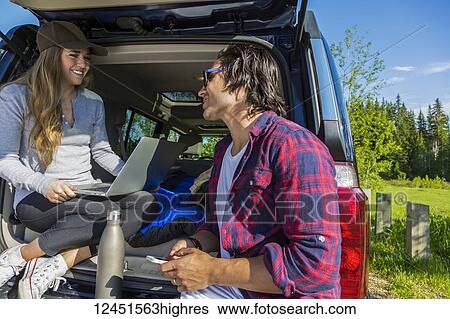 Young couple at their vehicle with the back open looking at a laptop computer; Edmonton, Alberta, Canada View Large Photo Image Stock Photograph - Young couple at their vehicle with the back open looking at a laptop computer; Edmonton, Alberta, Canada. Fotosearch