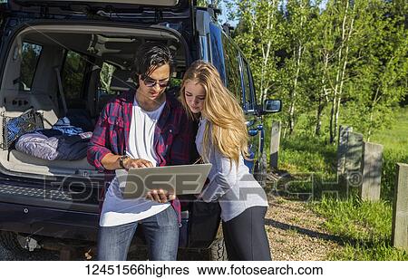Young couple at their vehicle with the back open looking at a laptop computer; Edmonton, Alberta, Canada View Large Photo Image Stock Photograph - Young couple at their vehicle with the back open looking at a laptop computer; Edmonton, Alberta, Canada. Fotosearch