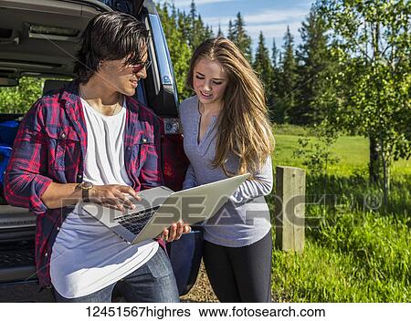 Young couple at their vehicle with the back open looking at a laptop computer; Edmonton, Alberta, Canada View Large Photo Image Stock Photograph - Young couple at their vehicle with the back open looking at a laptop computer; Edmonton, Alberta, Canada. Fotosearch