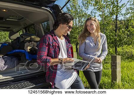 Stock Photograph - Young couple at their vehicle with the back open looking at a laptop computer; Edmonton, Alberta, Canada. Fotosearch
