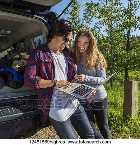 Young couple at their vehicle with the back open looking at a laptop computer; Edmonton, Alberta, Canada View Large Photo Image Stock Photograph - Young couple at their vehicle with the back open looking at a laptop computer; Edmonton, Alberta, Canada. Fotosearch