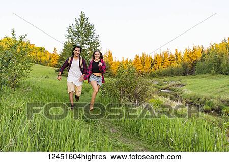 Young couple holding hands and running together down a trail in a city park; Edmonton, Alberta, Canada View Large Photo Image Stock Photograph - Young couple holding hands and running together down a trail in a city park; Edmonton, Alberta, Canada. Fotosearch