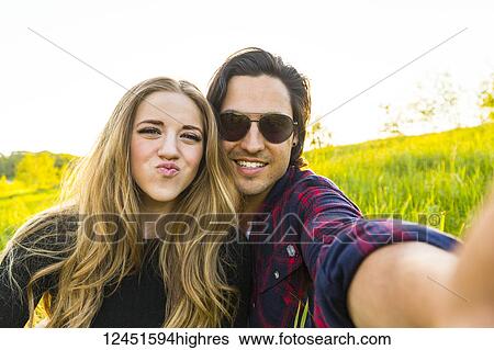 Young couple in a park posing for a self-portrait with their cell phone; Edmonton, Alberta, Canada View Large Photo Image Stock Photograph - Young couple in a park posing for a self-portrait with their cell phone; Edmonton, Alberta, Canada. Fotosearch