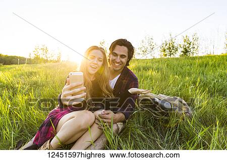 Young couple in a park posing for a self-portrait with their cell phone; Edmonton, Alberta, Canada View Large Photo Image Stock Photograph - Young couple in a park posing for a self-portrait with their cell phone; Edmonton, Alberta, Canada. Fotosearch