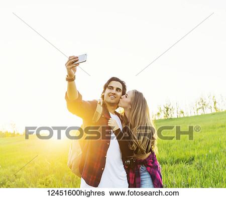 Stock Photograph - Young couple in a park posing for a self-portrait with their cell phone; Edmonton, Alberta, Canada. Fotosearch