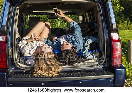 Young couple laying in the back of their packed vehicle on a road trip, showing their boots and using their cell phone; Edmonton, Alberta, Canada View Large Photo Image Stock Photograph - Young couple laying in the back of their packed vehicle on a road trip, showing their boots and using their cell phone; Edmonton, Alberta, Canada. Fotosearch