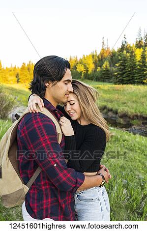 Stock Photograph - Young couple standing in a park in an embrace during a hike in autumn; Edmonton, Alberta, Canada. Fotosearch