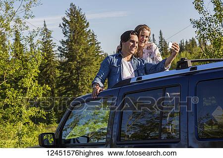 Young couple taking self-portraits with a cell phone while standing up in their sunroof of their vehicle; Edmonton, Alberta, Canada View Large Photo Image Stock Photograph - Young couple taking self-portraits with a cell phone while standing up in their sunroof of their vehicle; Edmonton, Alberta, Canada. Fotosearch