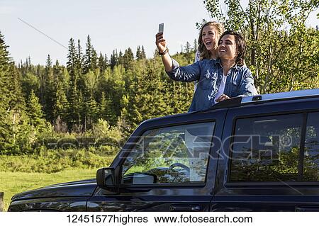 Young couple taking self-portraits with a cell phone while standing up in their sunroof of their vehicle; Edmonton, Alberta, Canada View Large Photo Image Stock Photograph - Young couple taking self-portraits with a cell phone while standing up in their sunroof of their vehicle; Edmonton, Alberta, Canada. Fotosearch