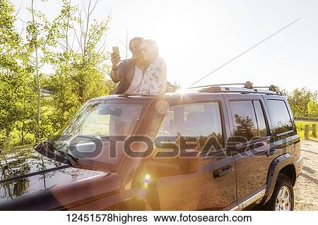 Young couple taking self-portraits with a cell phone while standing up in their sunroof of their vehicle; Edmonton, Alberta, Canada View Large Photo Image Stock Photograph - Young couple taking self-portraits with a cell phone while standing up in their sunroof of their vehicle; Edmonton, Alberta, Canada. Fotosearch