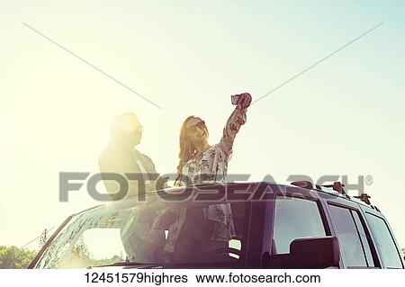 Stock Photograph - Young couple taking self-portraits with a cell phone while standing up in their sunroof of their vehicle; Edmonton, Alberta, Canada. Fotosearch