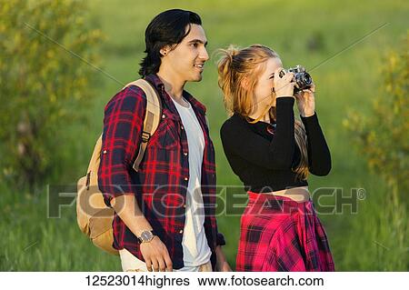 Stock Photograph - Young couple walking together in a city park pause to take a picture with a camera; Edmonton, Alberta, Canada. Fotosearch
